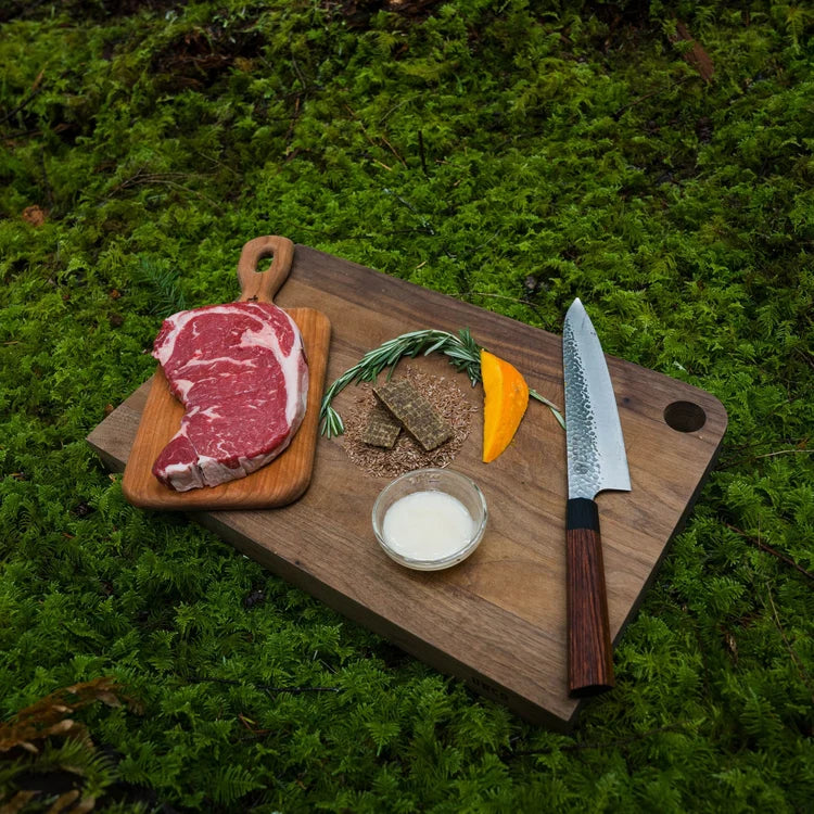 Raw beef steak on wooden board with rosemary, spices, and knife for Fraps Backcountry Beef Breakable Dog Treat Bar.