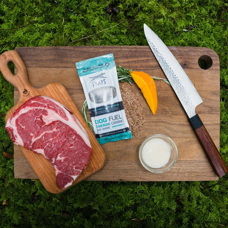 Fraps Backcountry Beef Breakable Dog Treat Bar package beside a raw beef steak on a cutting board with rosemary.
