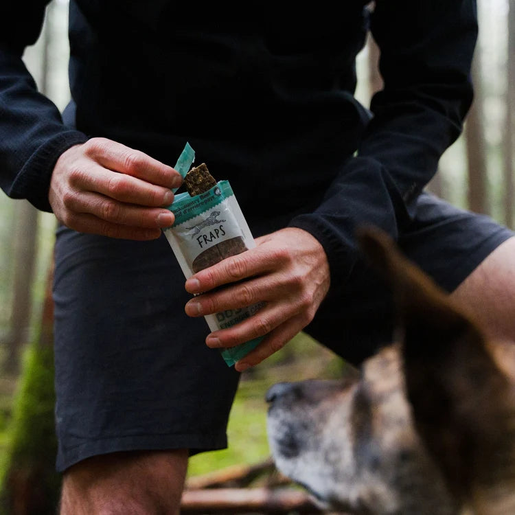 Opening a Fraps Backcountry Beef Breakable Dog Treat Bar for a dog outdoors.